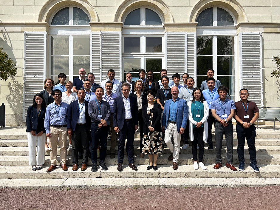 Group of professionals or researchers posing for a photograph outside of a building with large arched windows and stone exterior