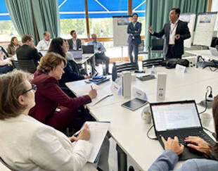 A group of people in a conference room, with two professors standing at the front, giving a presentation.