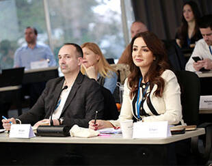 A group of people sitting at tables, likely in a classroom or conference room, engaged in a discussion or presentation.